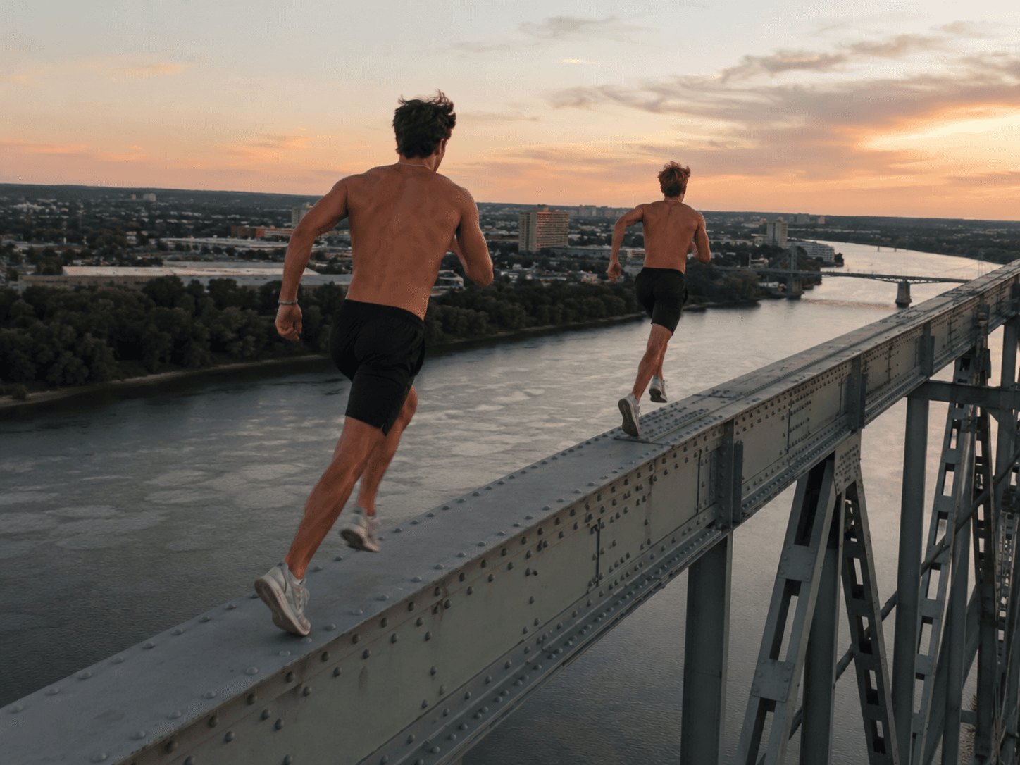 Two friends running across a bridge at sunset